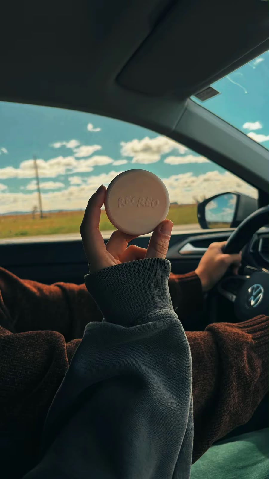 Una mano sostiene el Puck Recreo dentro de un auto, con el campo de fondo.